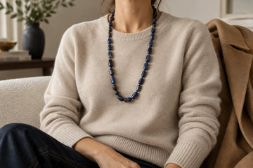 Long blue stone necklace worn over a fine oatmeal crew-neck sweater beside a camel coat