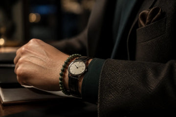 A small watch styled beside a restrained natural-stone bracelet under a tailored cuff