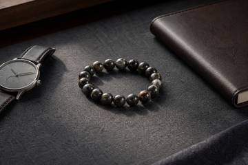 Dark natural stone bracelet styled beside a watch and notebook for men's everyday wear