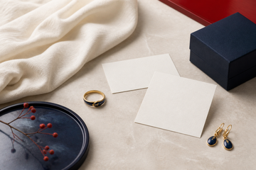 A restrained Qixi jewelry gift still life with a ring, earrings, natural cloth, and two blank cards